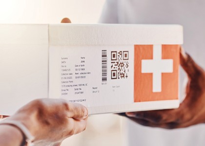 Two people exchanging a white box with a barcode and an orange plus sign on the side.
