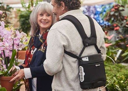 Two older people in a flower market, one is wearing a portable oxygen concentrator