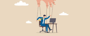 An illustration of a man at a desk with a puppeteer hand over him to symbolize mircomanagement